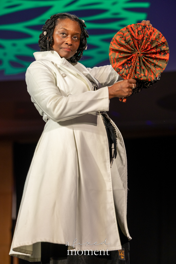 Participant in a white coat holding a fan on the runway at Brooklyn's 2026 People's Ball