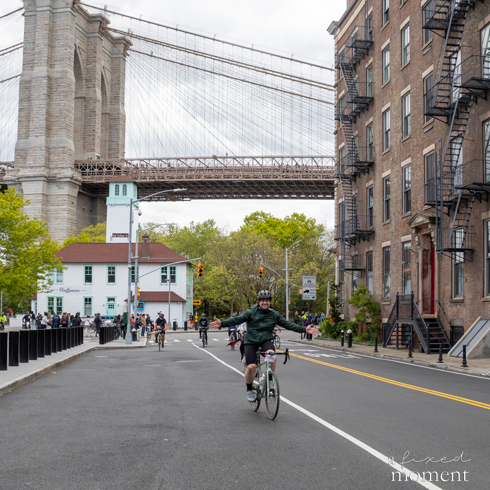 Cyclist rides with arms out near the Brooklyn Bridge in DUMBO during the 2026 Five Boro Bike Tour