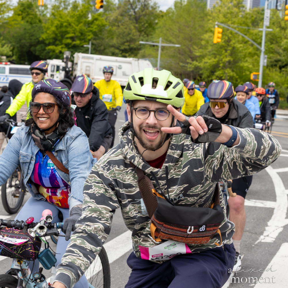 Cyclist in a camo hoodie flashes a peace sign during the 2026 Five Boro Bike Tour