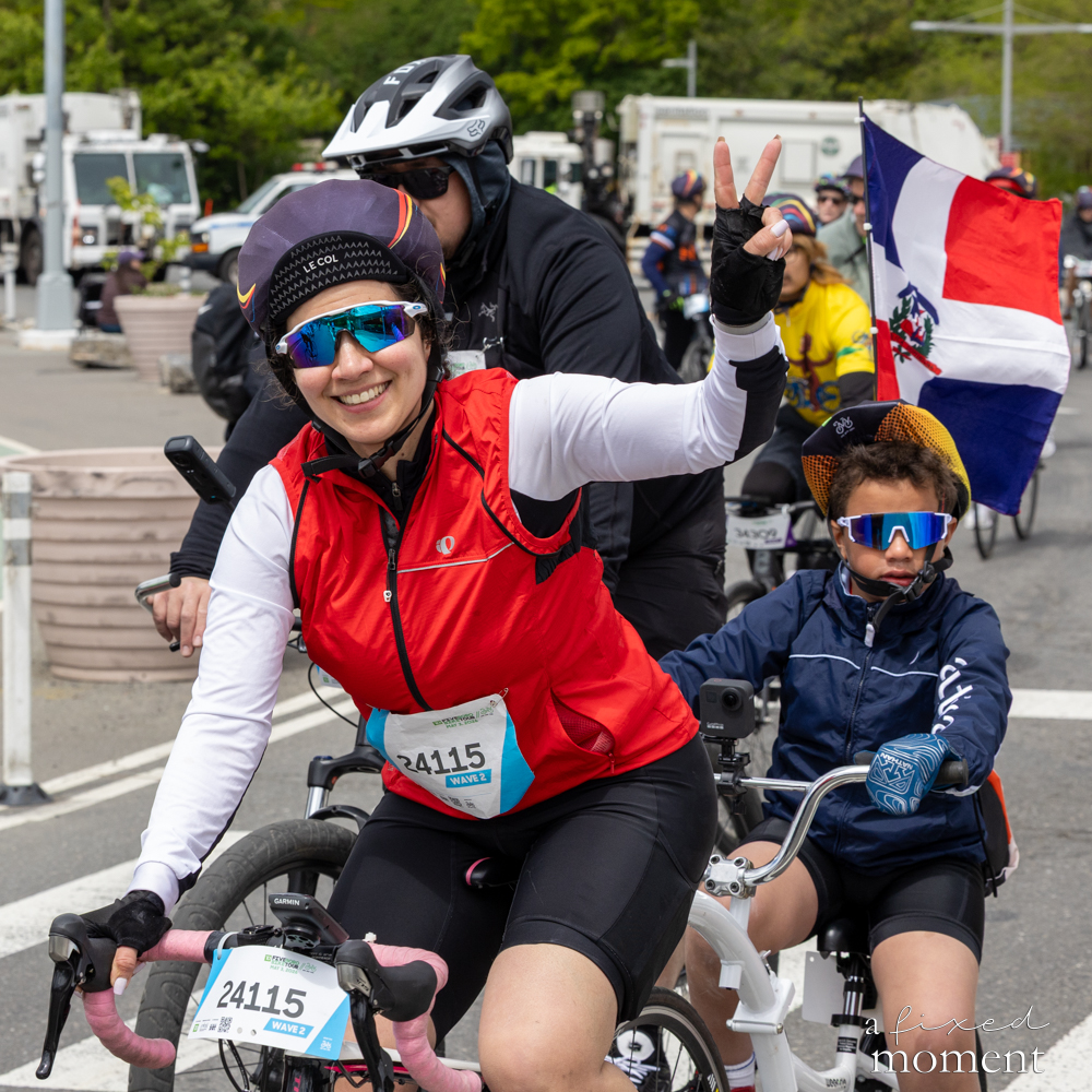 Cyclist with a Dominican flag and a child flashes a peace sign at the Five Boro Bike Tour