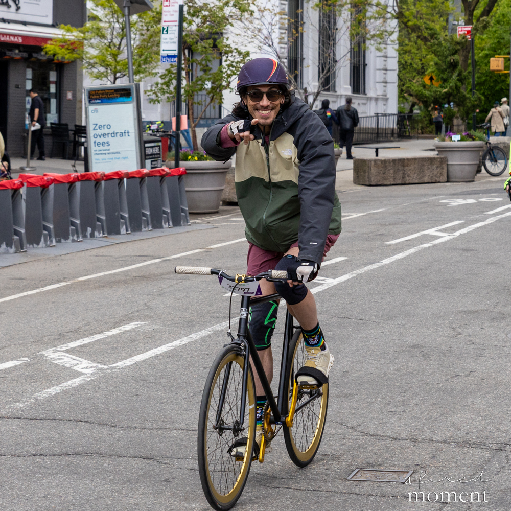 Cyclist points at the camera on a city street during the 2026 Five Boro Bike Tour