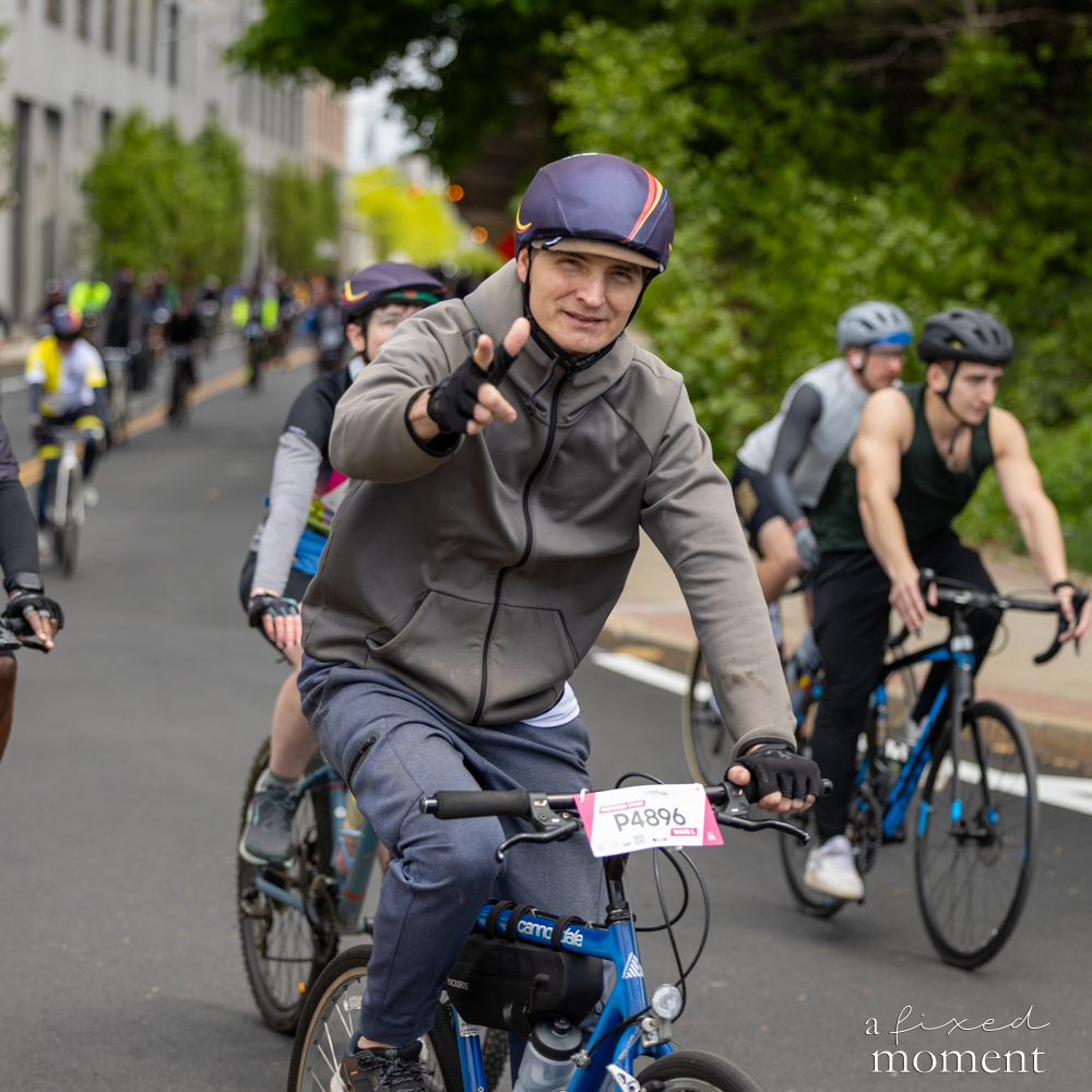 Cyclist points at the camera during a group ride at the 2026 Five Boro Bike Tour