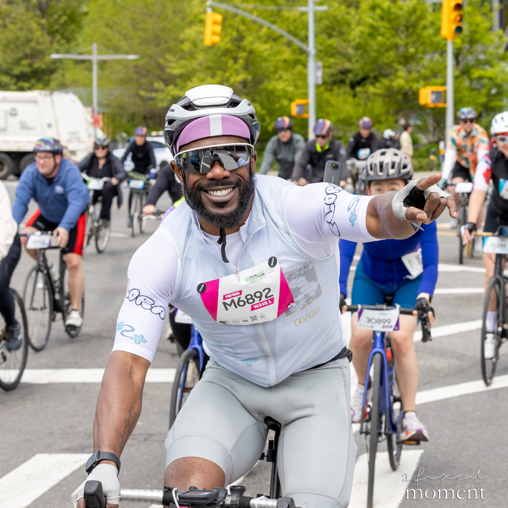 Cyclist in a white kit points forward during a group ride at the Five Boro Bike Tour
