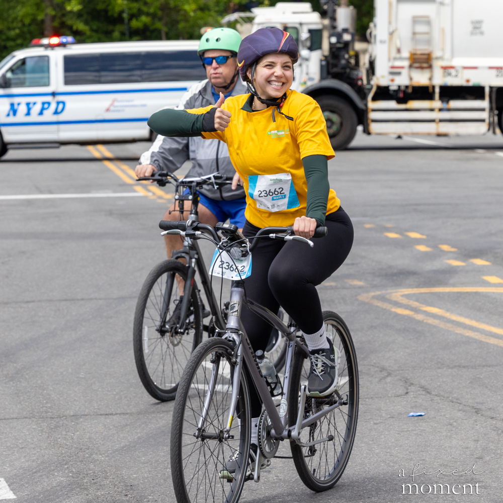 Cyclist in a yellow shirt gives a thumbs up at an intersection during the Five Boro Bike Tour