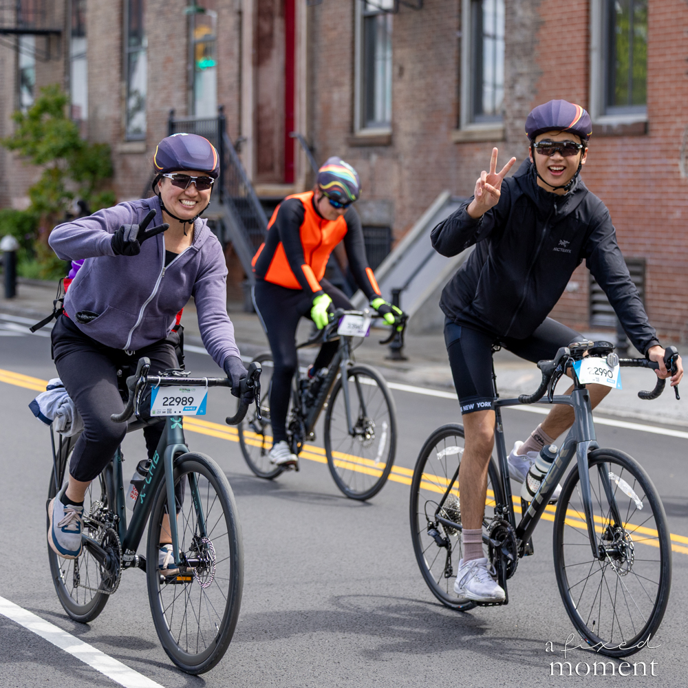Cyclists flash peace signs while riding down a city street