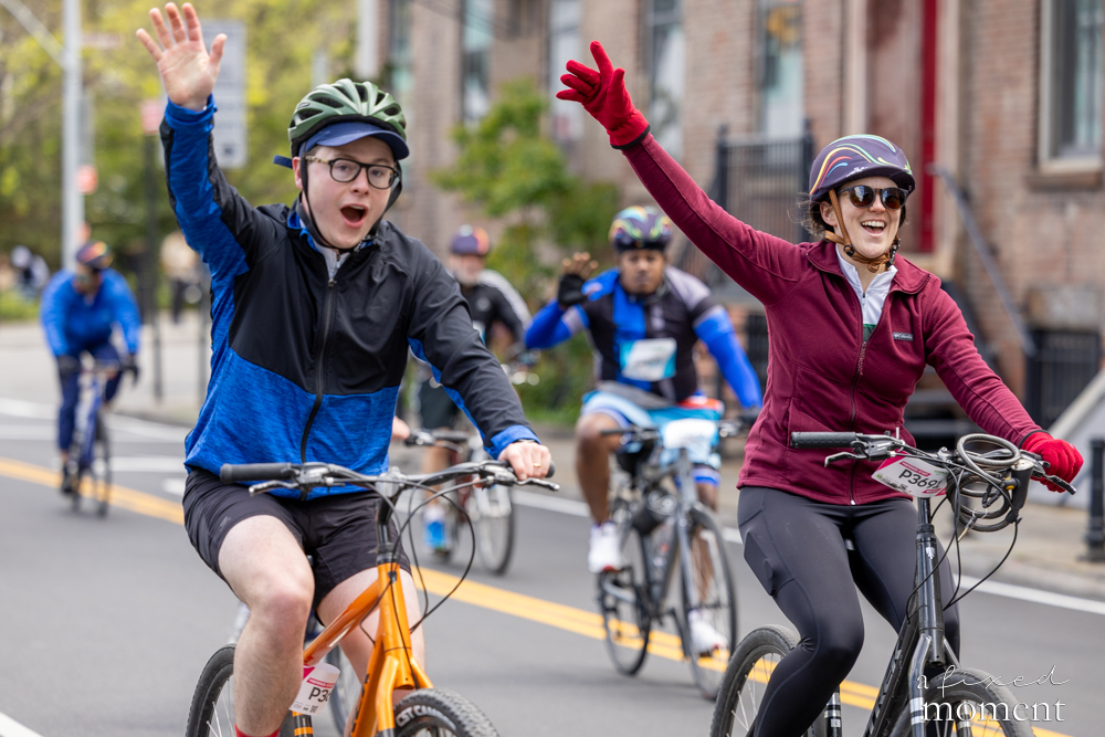 Cyclists wave and cheer on a city street during the 2026 Five Boro Bike Tour