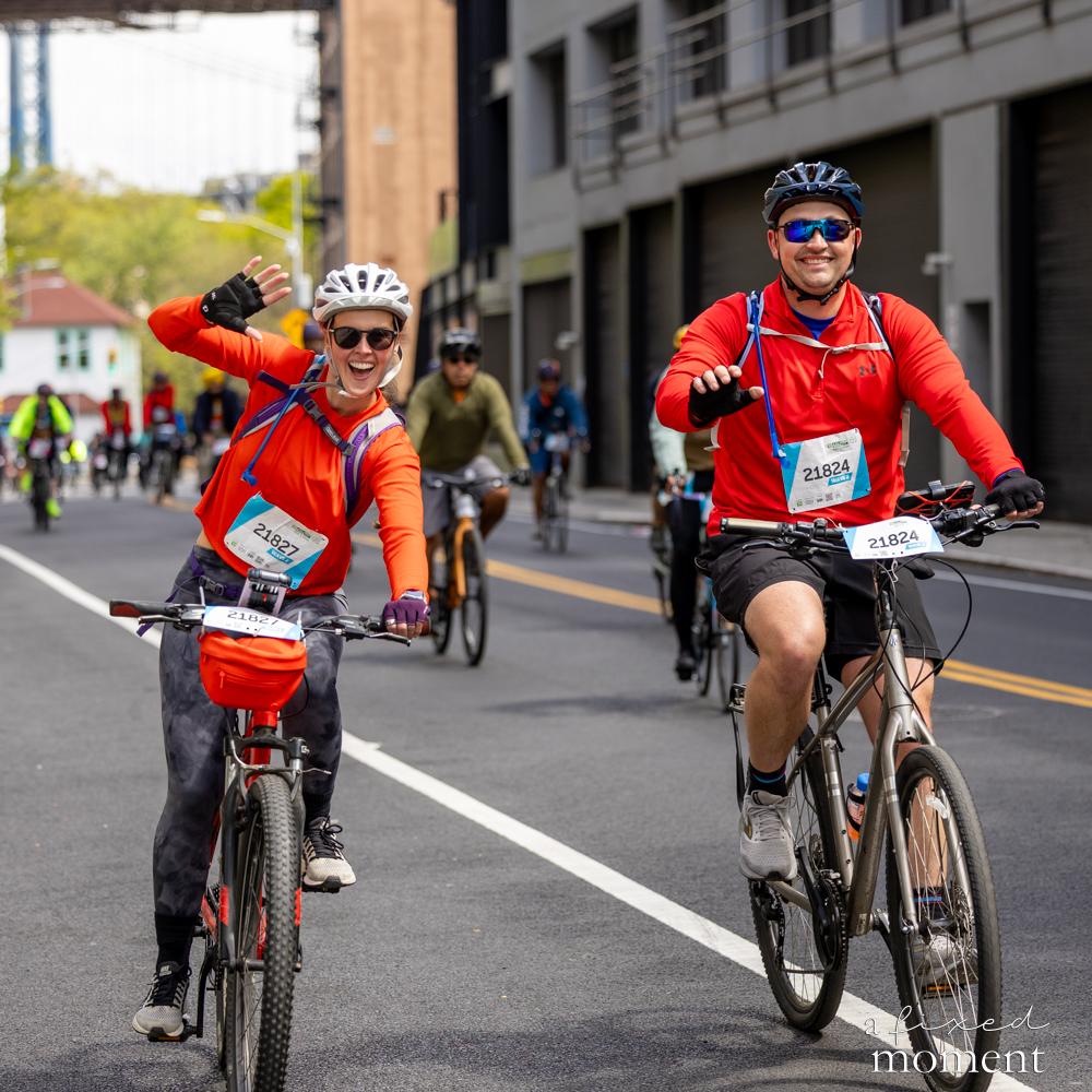 Cyclists in red outfits wave to the camera during the 2026 Five Boro Bike Tour