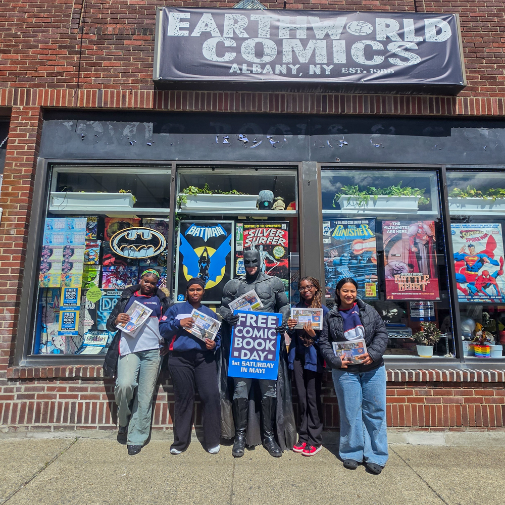 Batman cosplayer poses with attendees outside Earthworld Comics during Free Comic Book Day