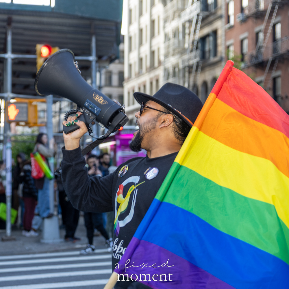 A participant holds a rainbow flag and speaks through a megaphone during the May Day Protest in New York City on May 1, 2026