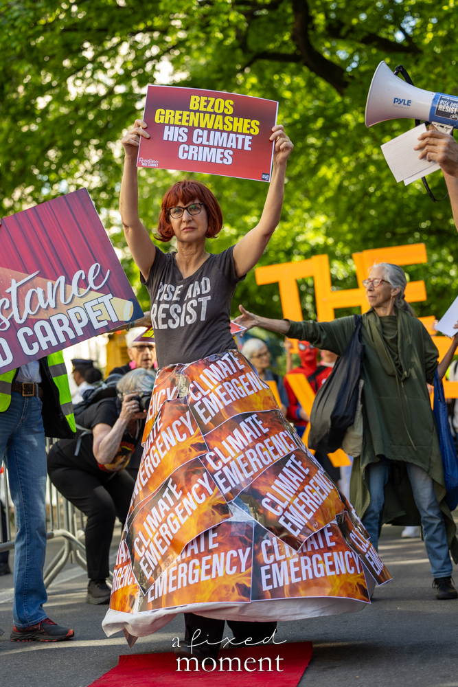 Rise and Resist protester holds a sign reading Bezos greenwashes his climate crimes outside the Met Gala in New York City
