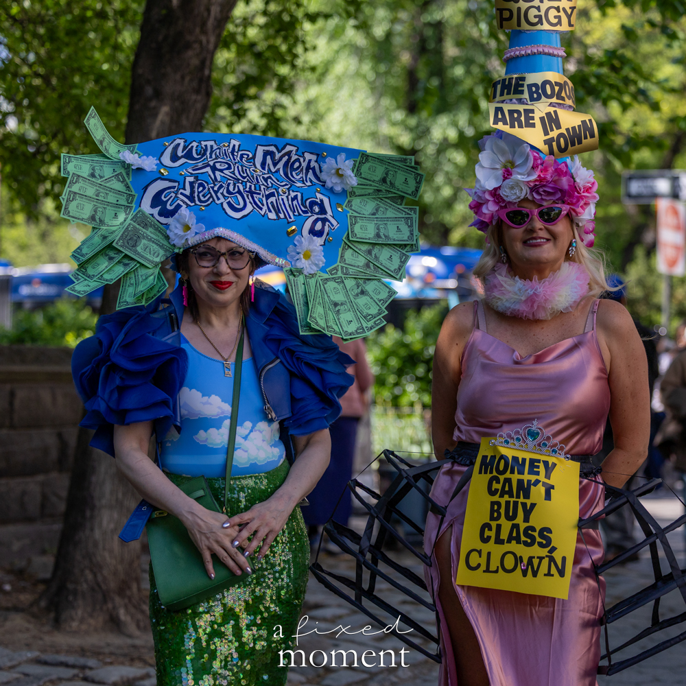 Costumed protesters hold signs reading Money Can't Buy Class Clown and White Men Are Clowning Everything outside the Met Gala
