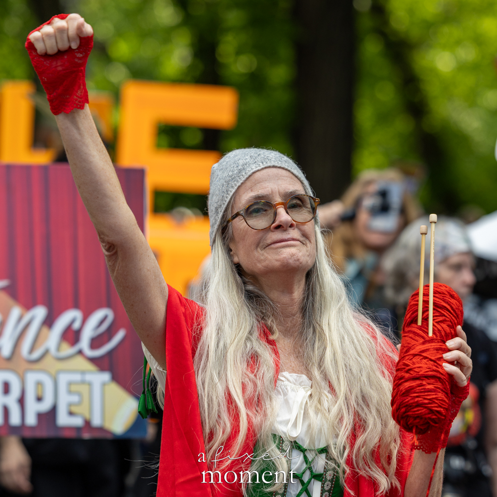 Participant raises a fist while holding yarn during the Resistance Red Carpet protest outside the Met Gala