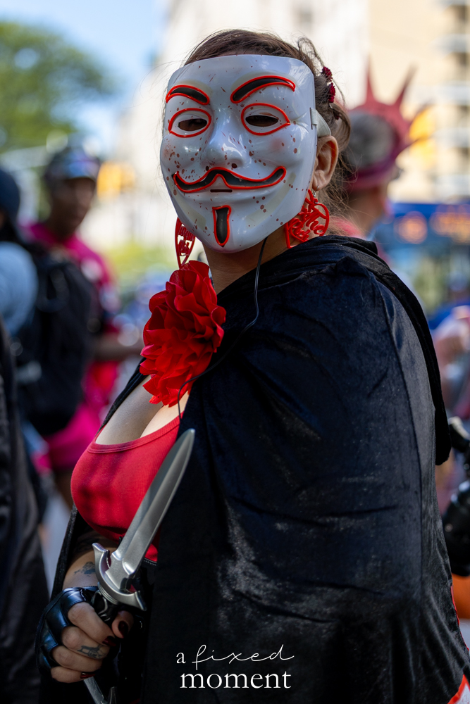Close portrait of a masked participant in a red and black costume outside the Met Gala