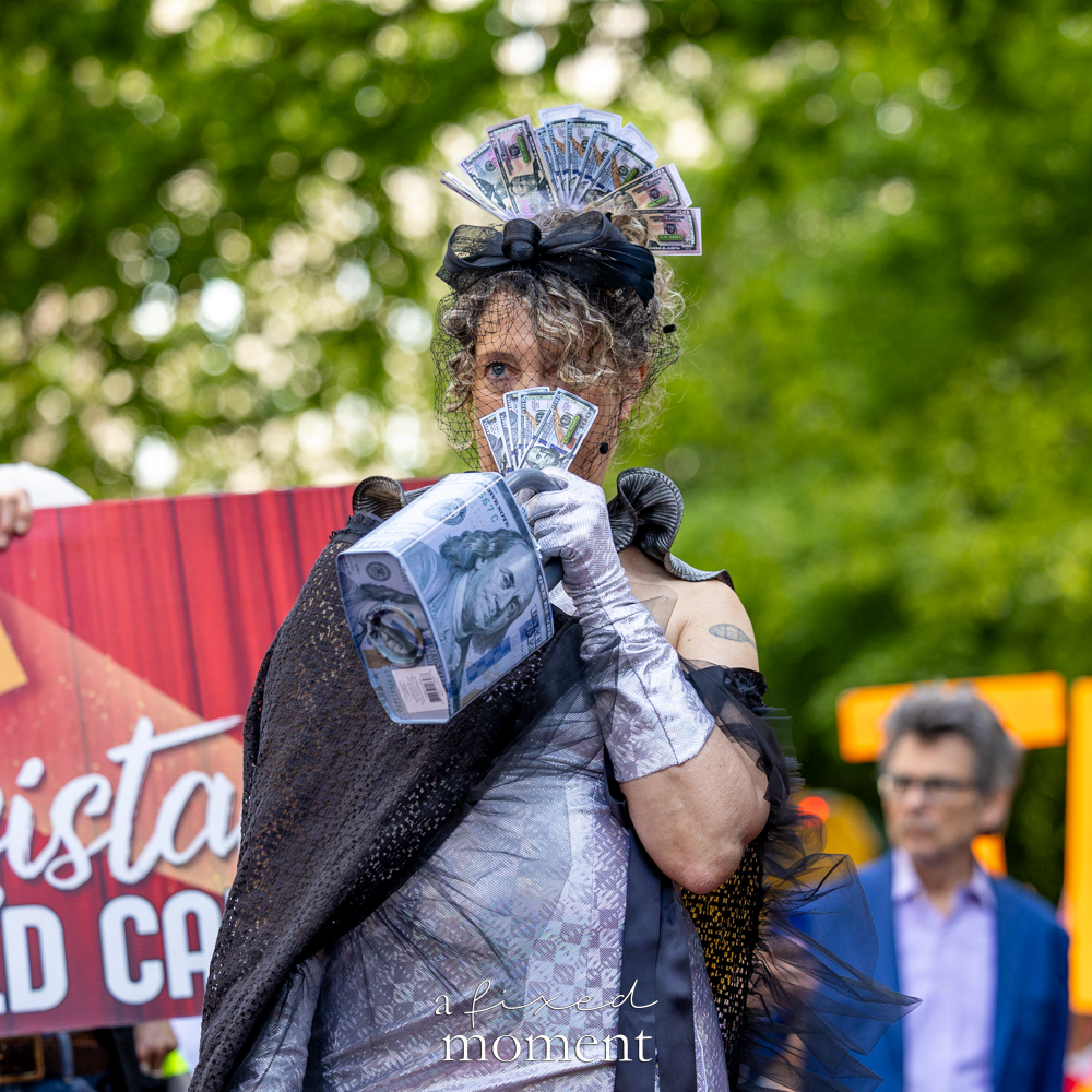 Money-themed costumed protester with fake bills and silver gloves at the Resistance Red Carpet outside the Met Gala