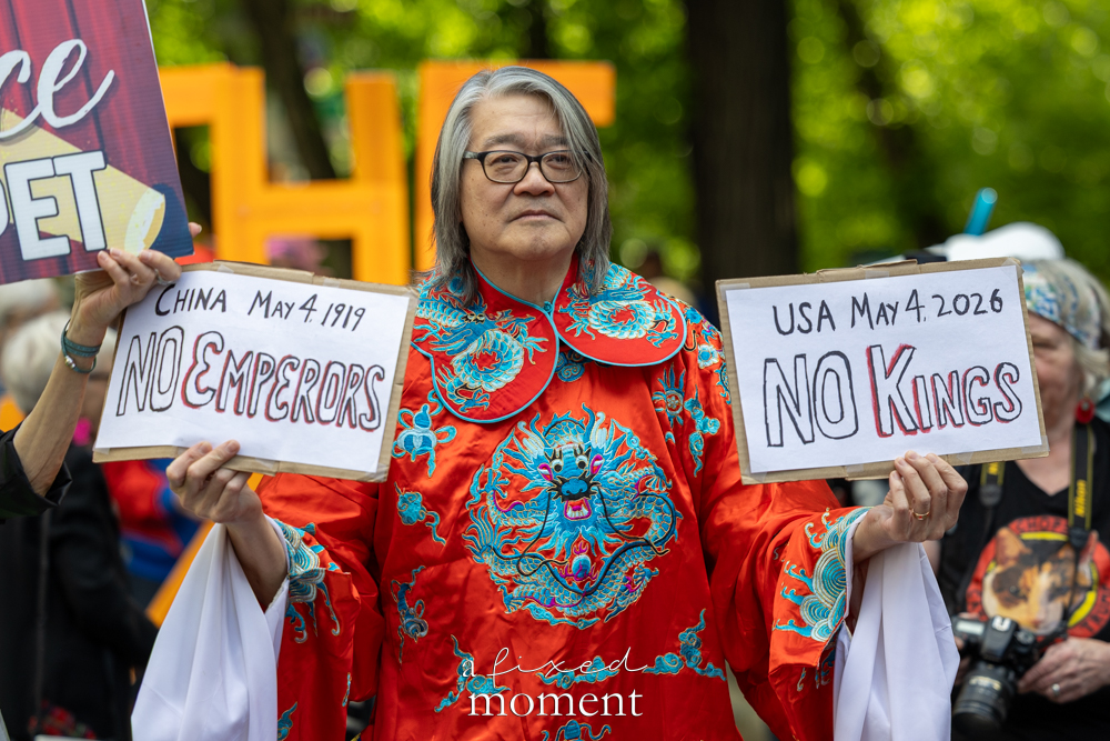 Participant in a red robe holds signs reading China May 4 1919 No Emperors and USA May 4 2026 No Kings outside the Met Gala