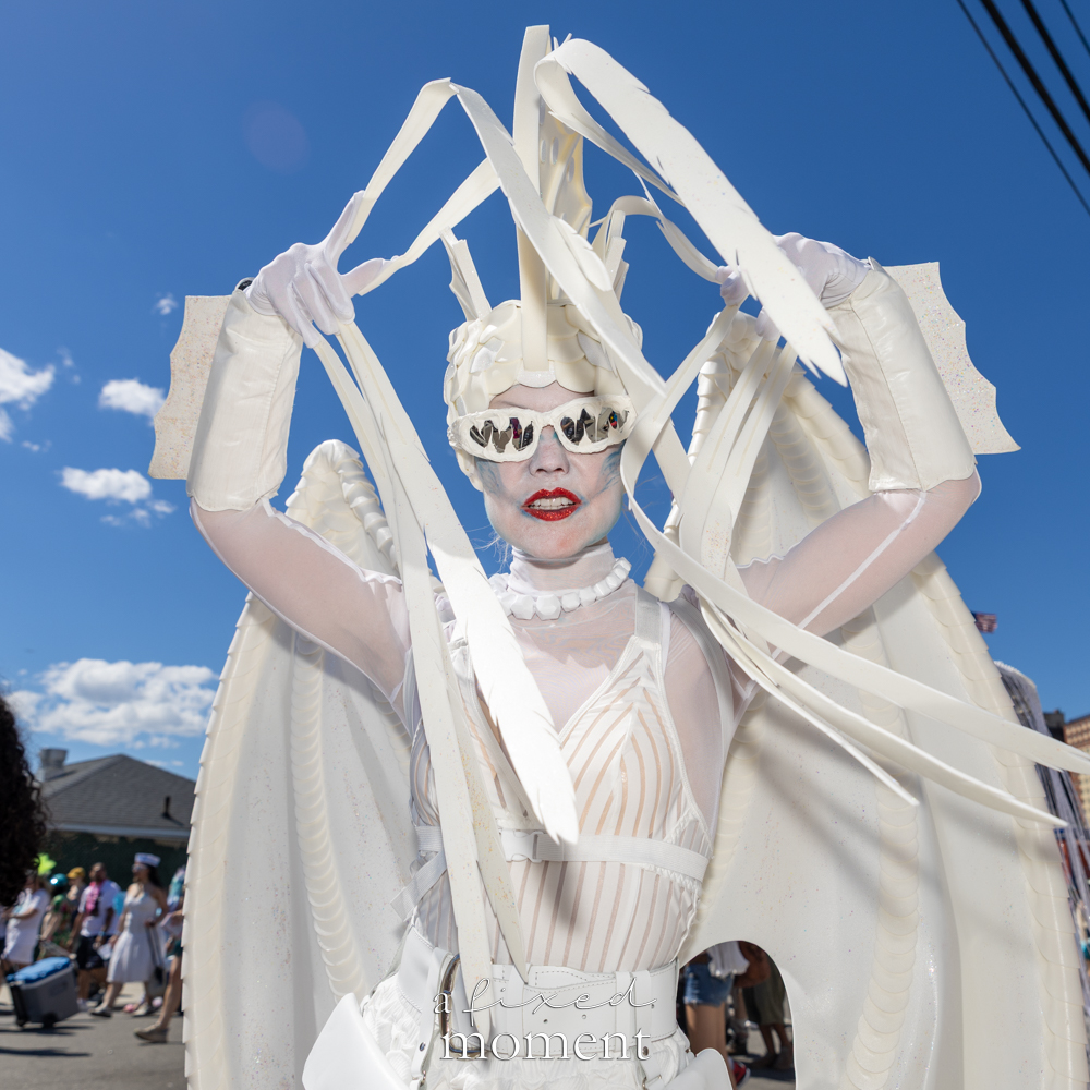 @summersparkles__ in a white sculptural sea-creature costume at the Mermaid Parade in Coney Island.