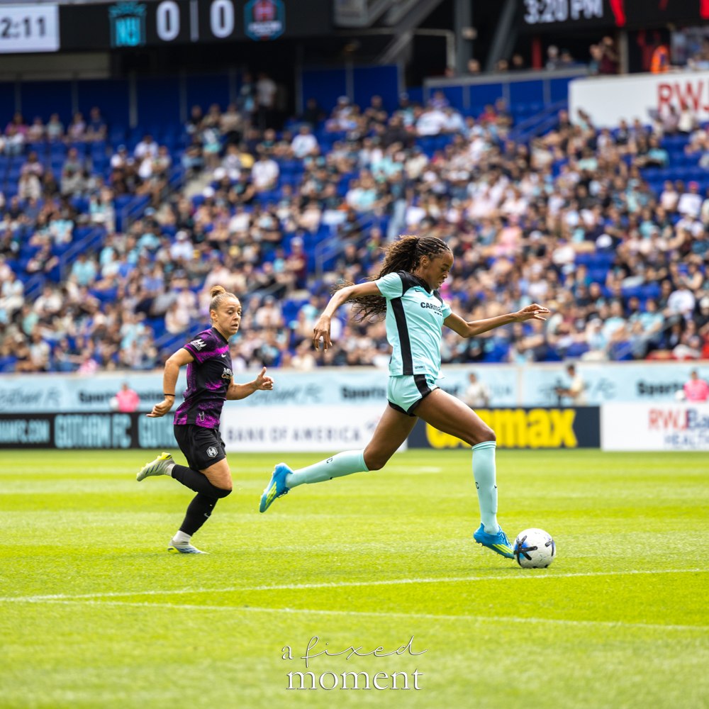 Gotham FC @gothamfc player in a light-blue kit sprinting with the ball as a Houston Dash @houstondash player chases behind her on the field.