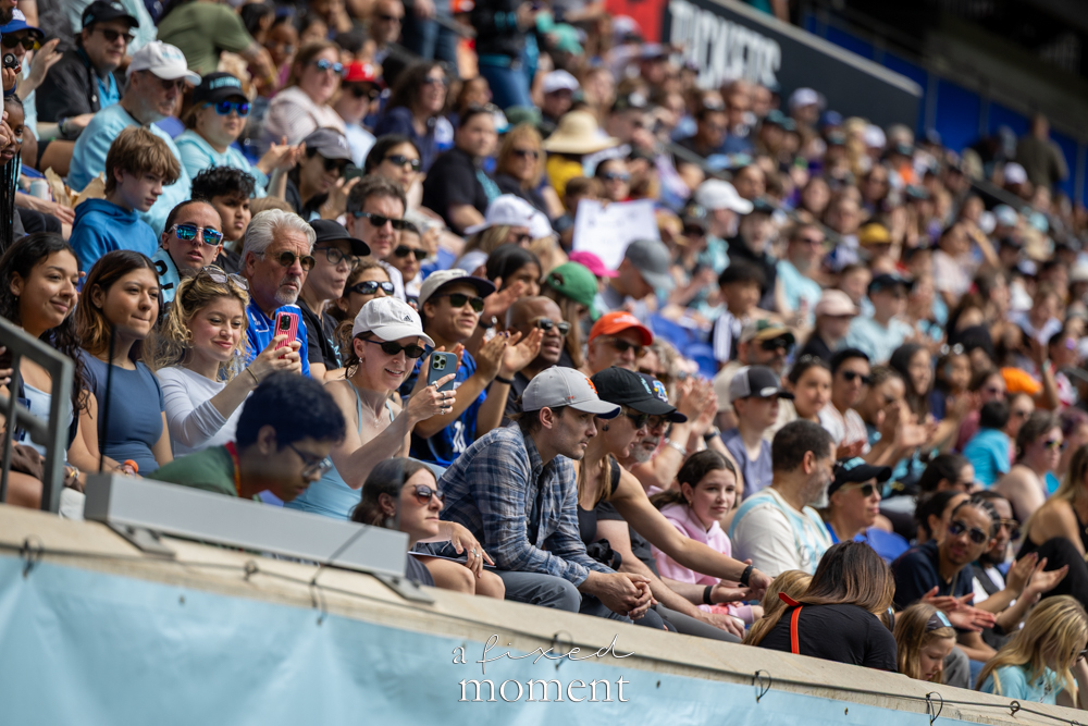 Gotham FC @gothamfc supporters sitting in the stands, clapping and holding up phones during a soccer match.