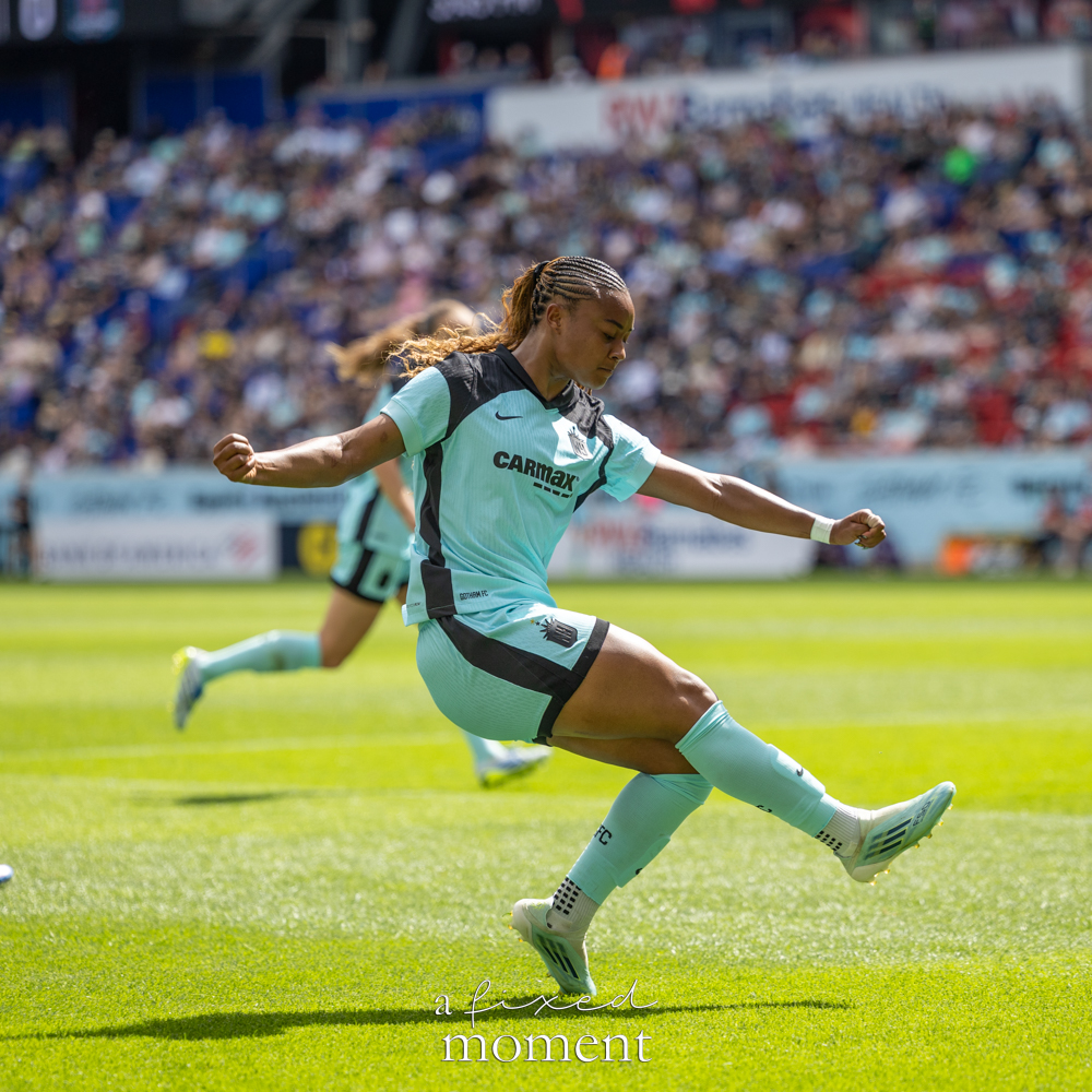 Gotham FC @gothamfc player in a light-blue kit kicking the ball on the field with a blurred crowd in the background.