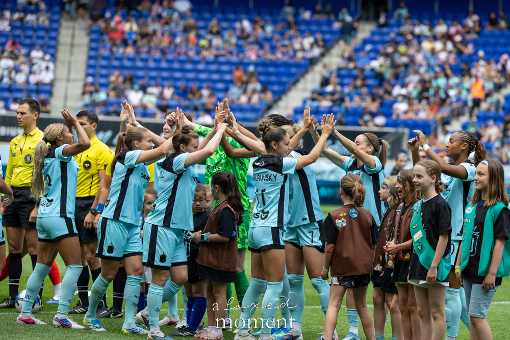 Gotham FC players in light-blue uniforms high-five Girl Scouts and youth participants on the field before a soccer match.