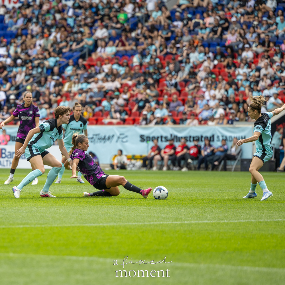 Gotham FC @gothamfc player in a light-blue kit shooting the ball as a Houston Dash @houstondash defender in a black-and-purple kit slides in front of her.