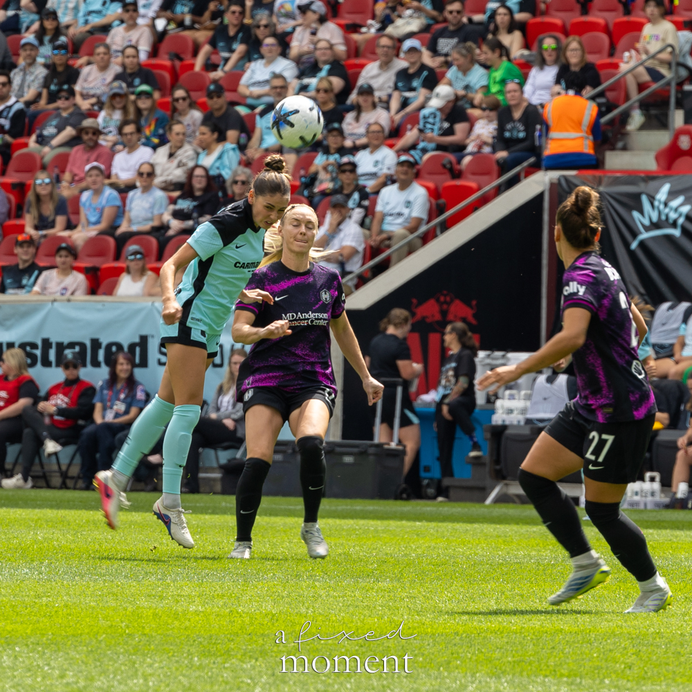 Gotham FC @gothamfc player in a light-blue kit challenging a Houston Dash @houstondash player in a black-and-purple kit for a header on the field.
