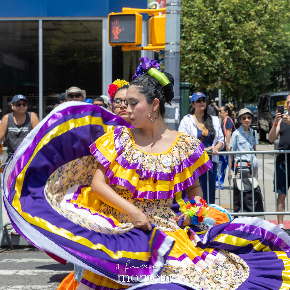 A folkloric dancer performs in a purple and yellow dress during Queens Pride.