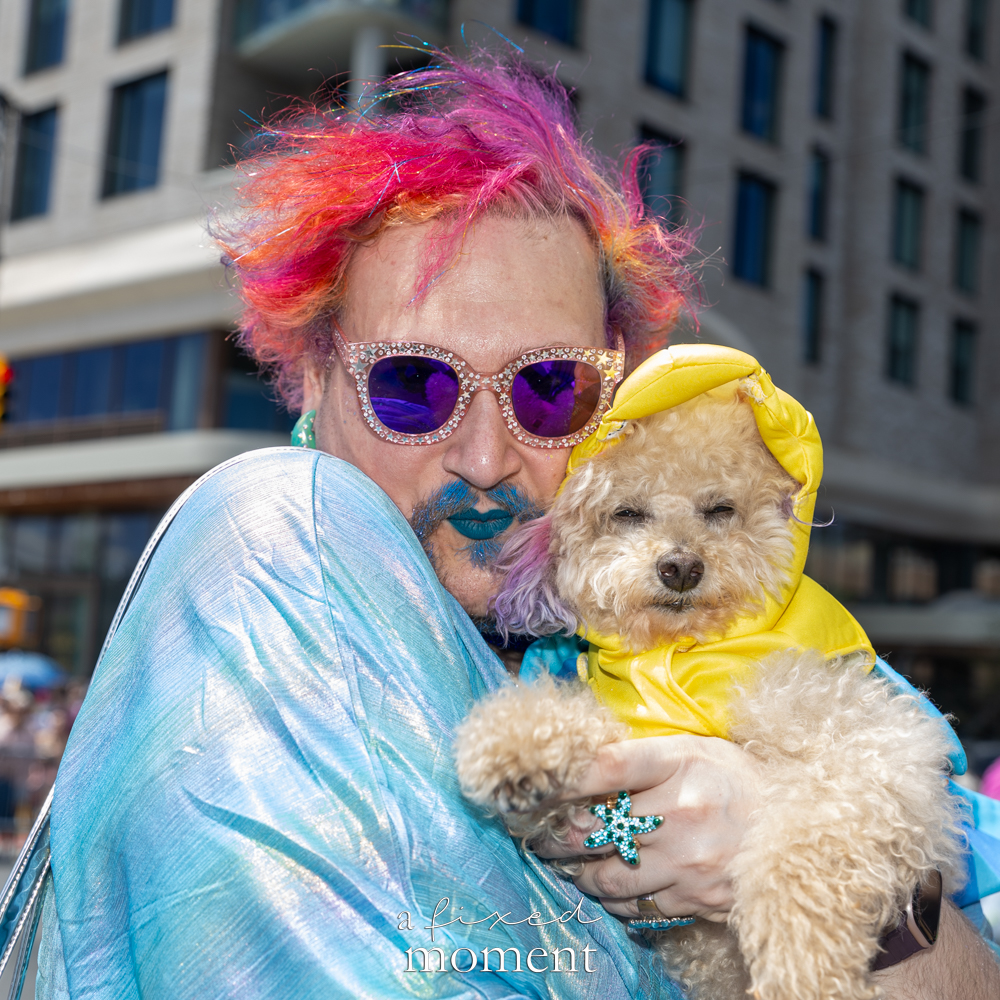 A colorful paradegoer holds a small dog in a yellow hood during the Mermaid Parade.