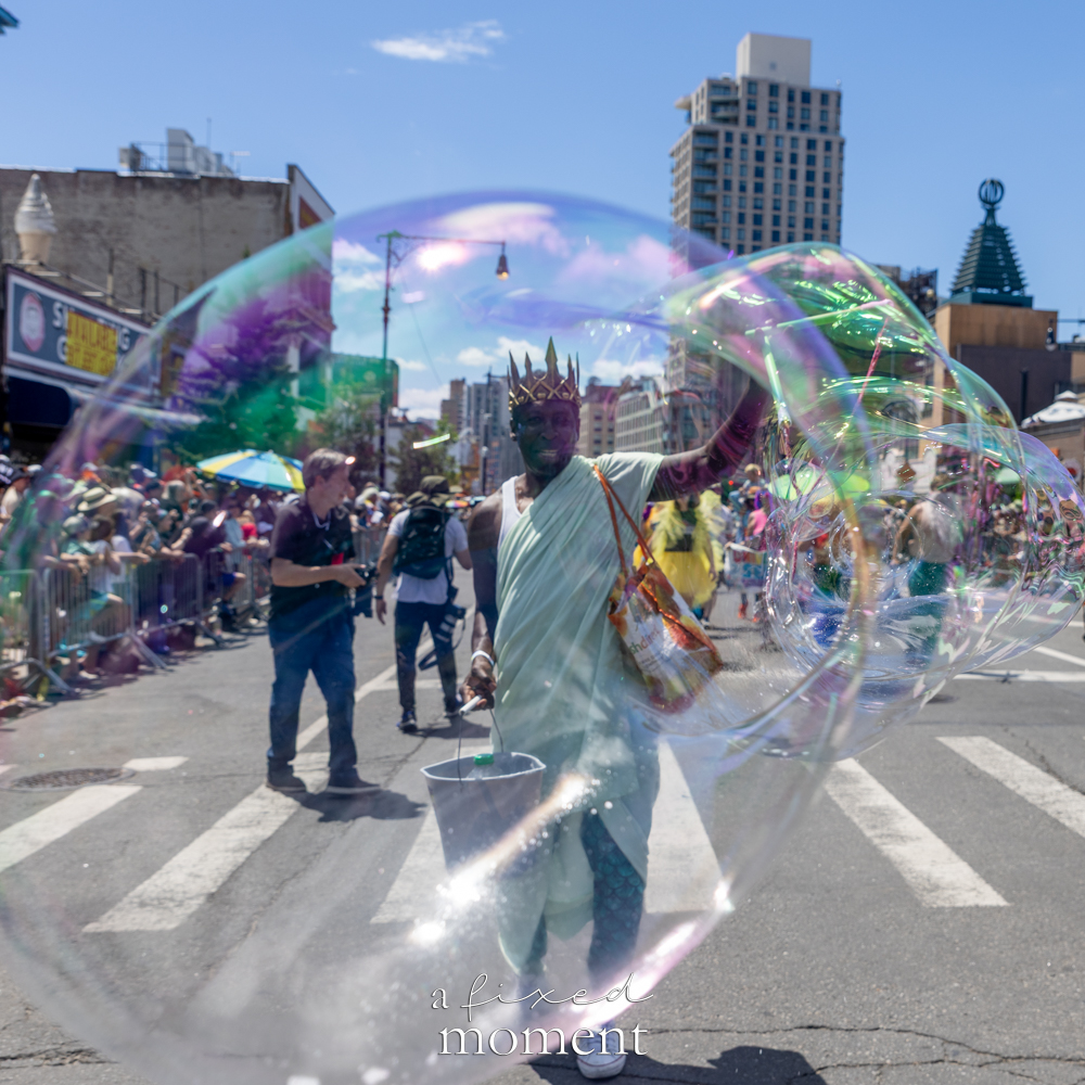 A crowned performer creates a giant iridescent soap bubble during the Mermaid Parade in Coney Island.