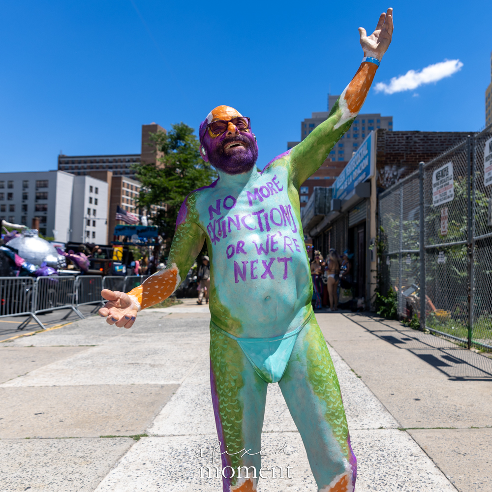 @hardybrooklyn.nyc wears body paint reading NO MORE EXTINCTION OR WE’RE NEXT during the Mermaid Parade.