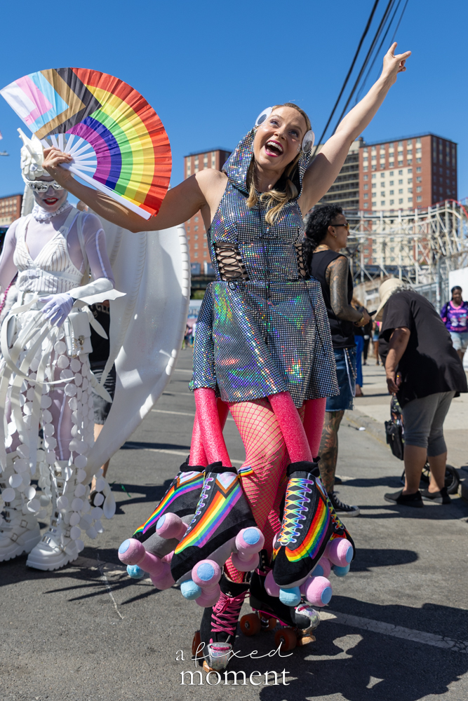 Rainbow roller skater with fan and oversized skate props at the Mermaid Parade.