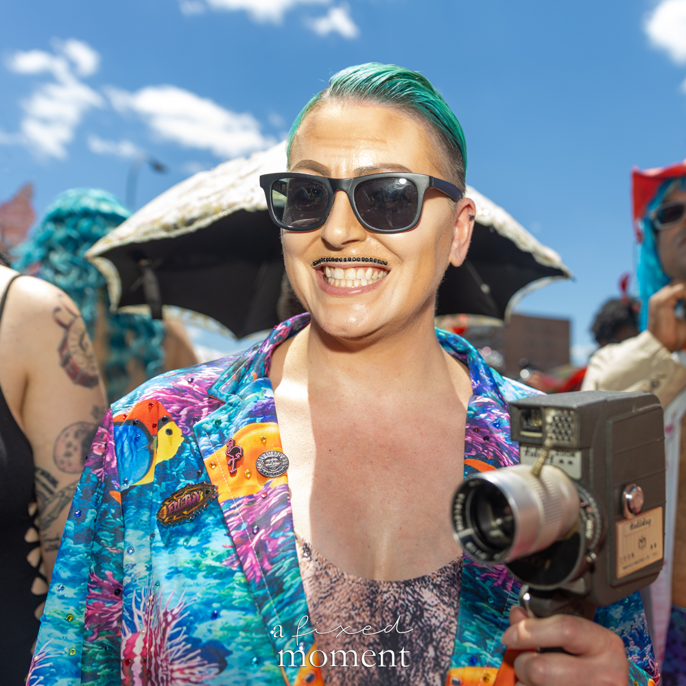 Turquoise-haired participant with vintage camera at the Mermaid Parade.