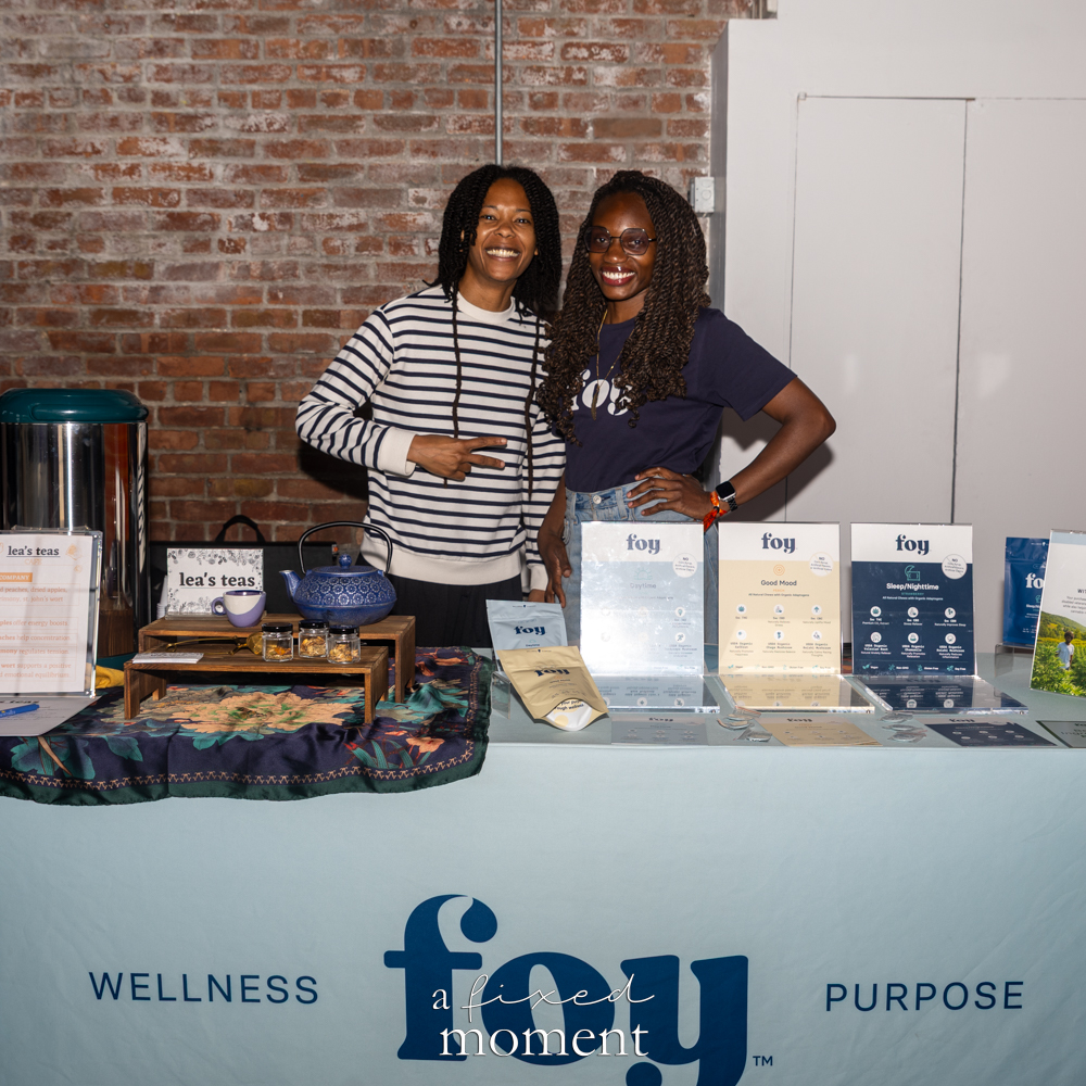 Foy vendors stand behind a wellness product and tea display.