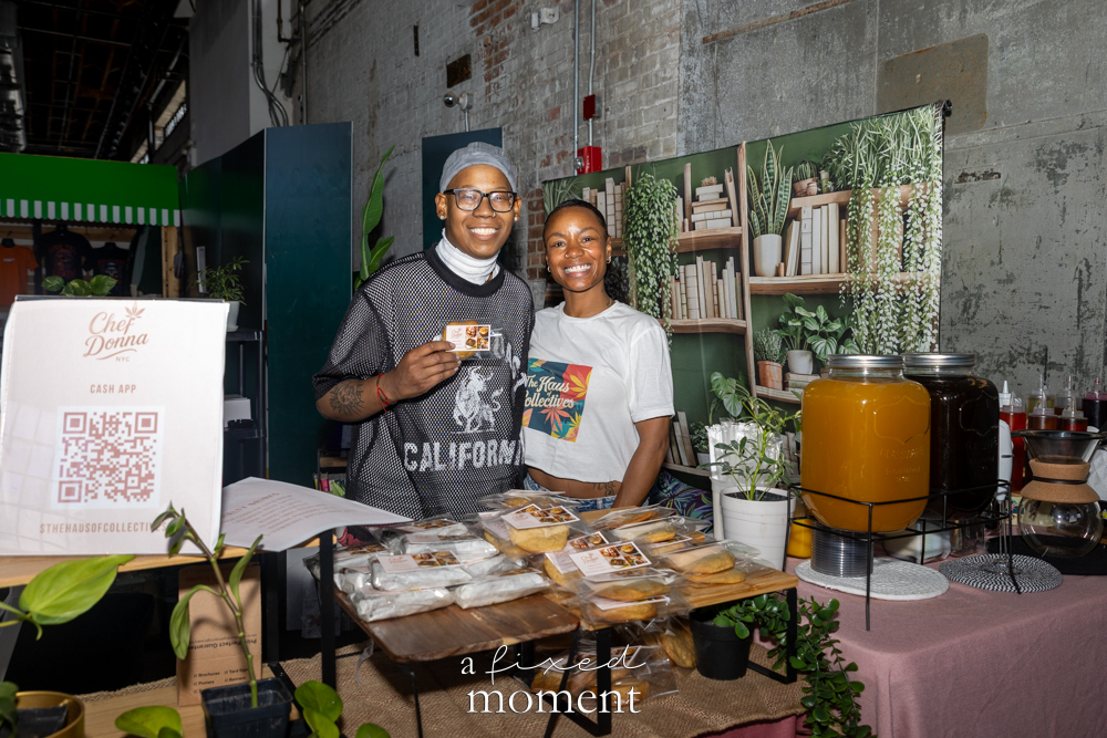 Vendors stand behind a booth with packaged goods, plants and drink dispensers.