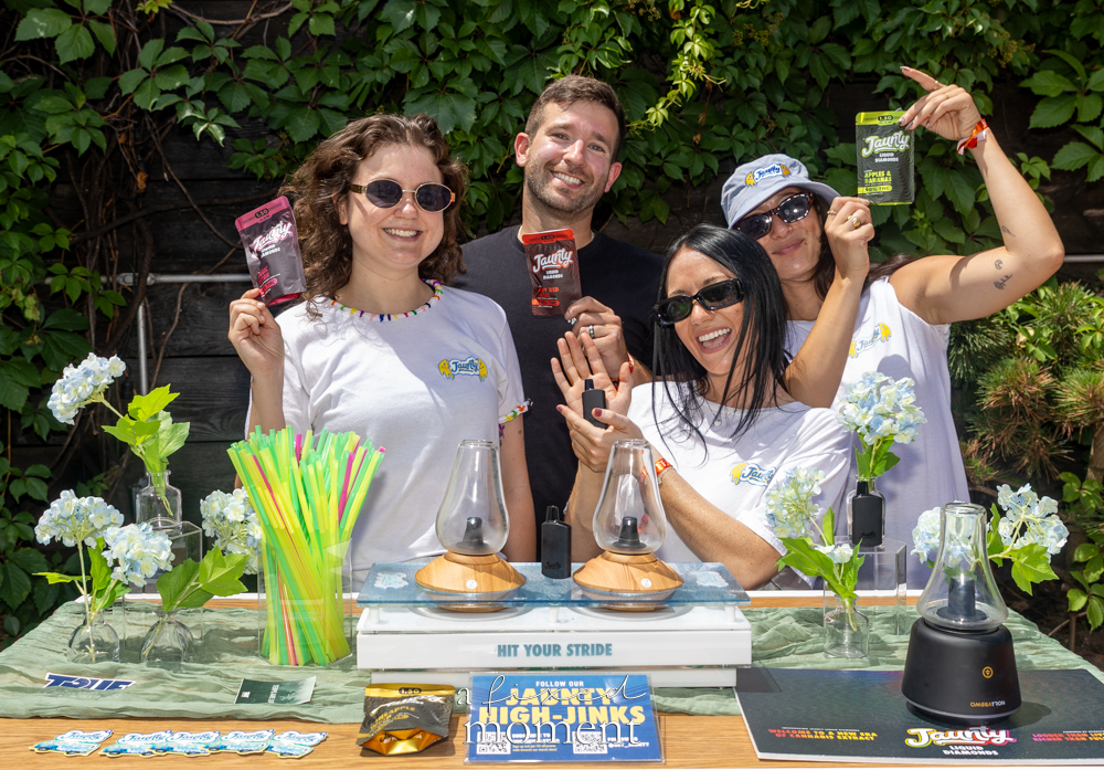 Four Jaunty representatives smile behind a cannabis vendor table with branded packages, colorful straws, flowers and display pieces.