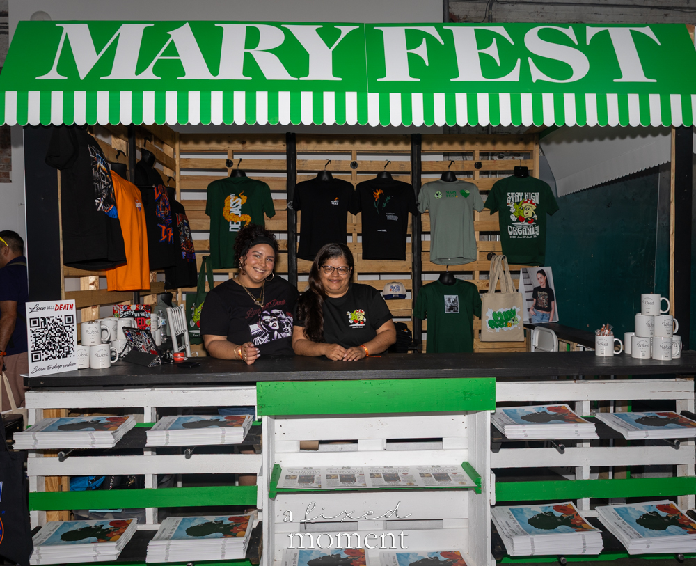 Love Till Death vendors sit behind a merchandise booth with apparel and accessories.