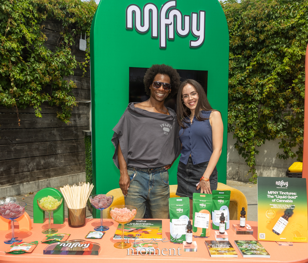 Two MFNY representatives stand behind a cannabis vendor table with tinctures, product bags, brochures and a green MFNY backdrop.