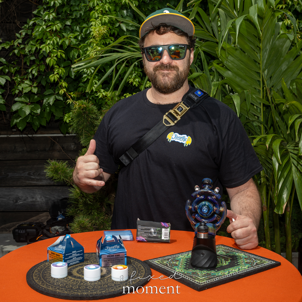 Vendor stands behind a table with Orian Glass and Jaunty products.