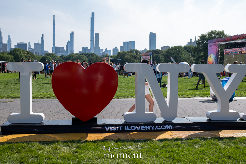 I Love New York display with World Cup watch party crowd and Manhattan skyline in Central Park