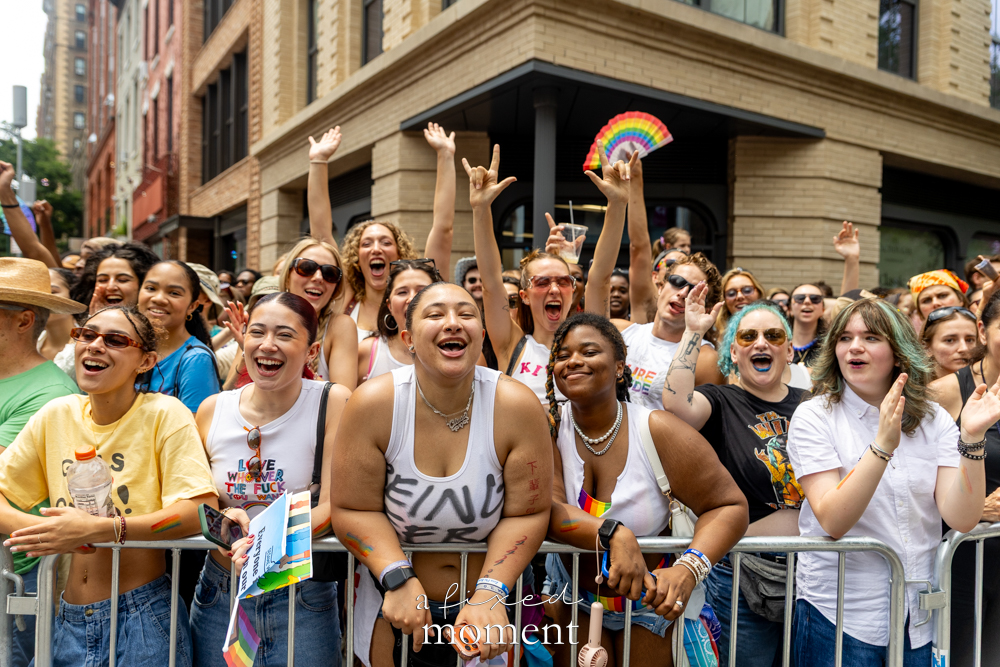 Cheering crowd behind barricade with Pride fan at NYC Pride March 2026