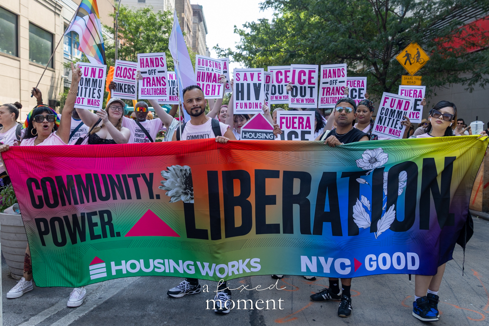 Housing Works Community Power Liberation banner at the 2026 Queer Liberation March with signs about housing HIV funding ICE Rikers and trans healthcare