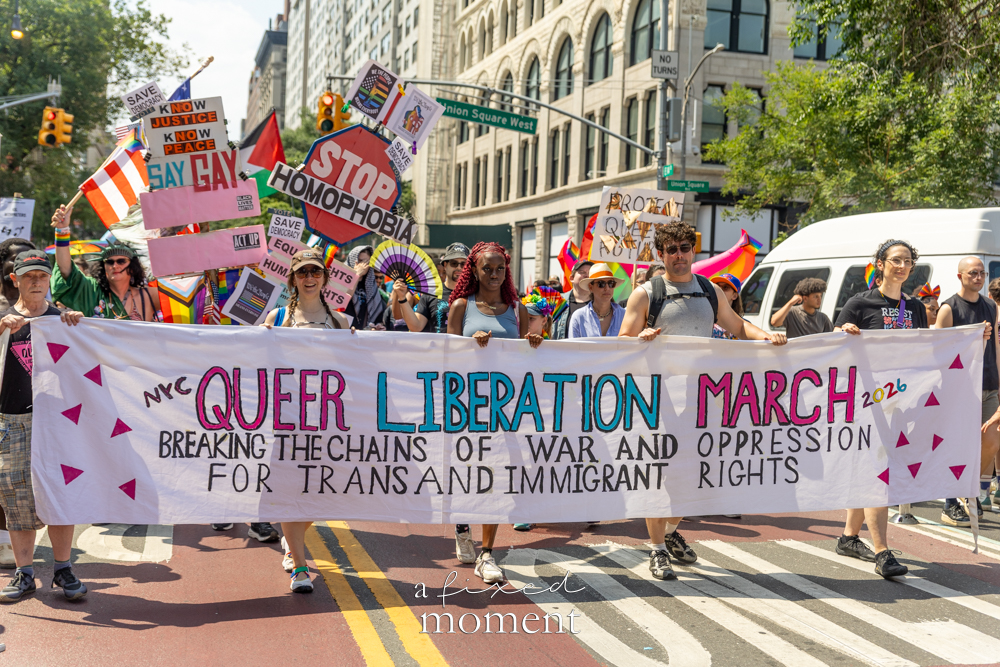 Front banner at the 2026 Queer Liberation March in Union Square with marchers holding protest signs and Pride flags in New York City