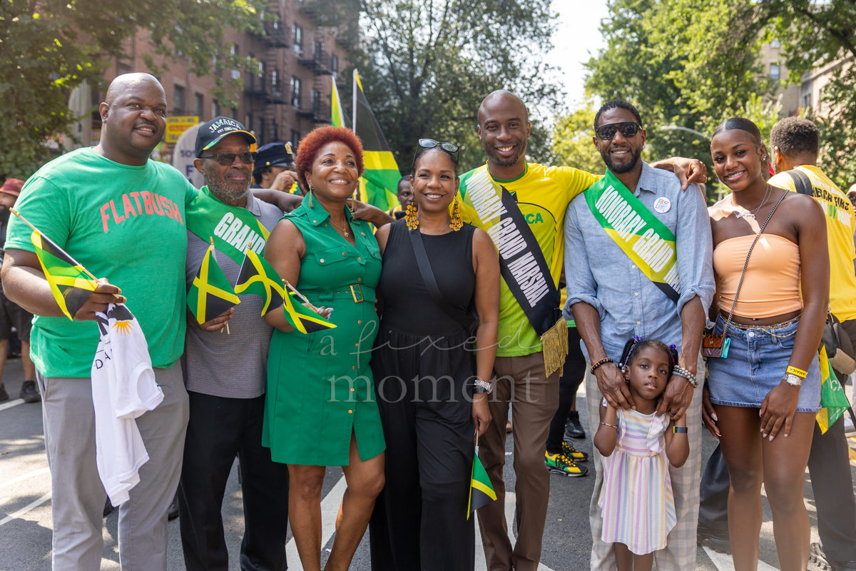 Grand marshals, honorary grand marshals and participants pose together with small Jamaican flags on a Brooklyn street