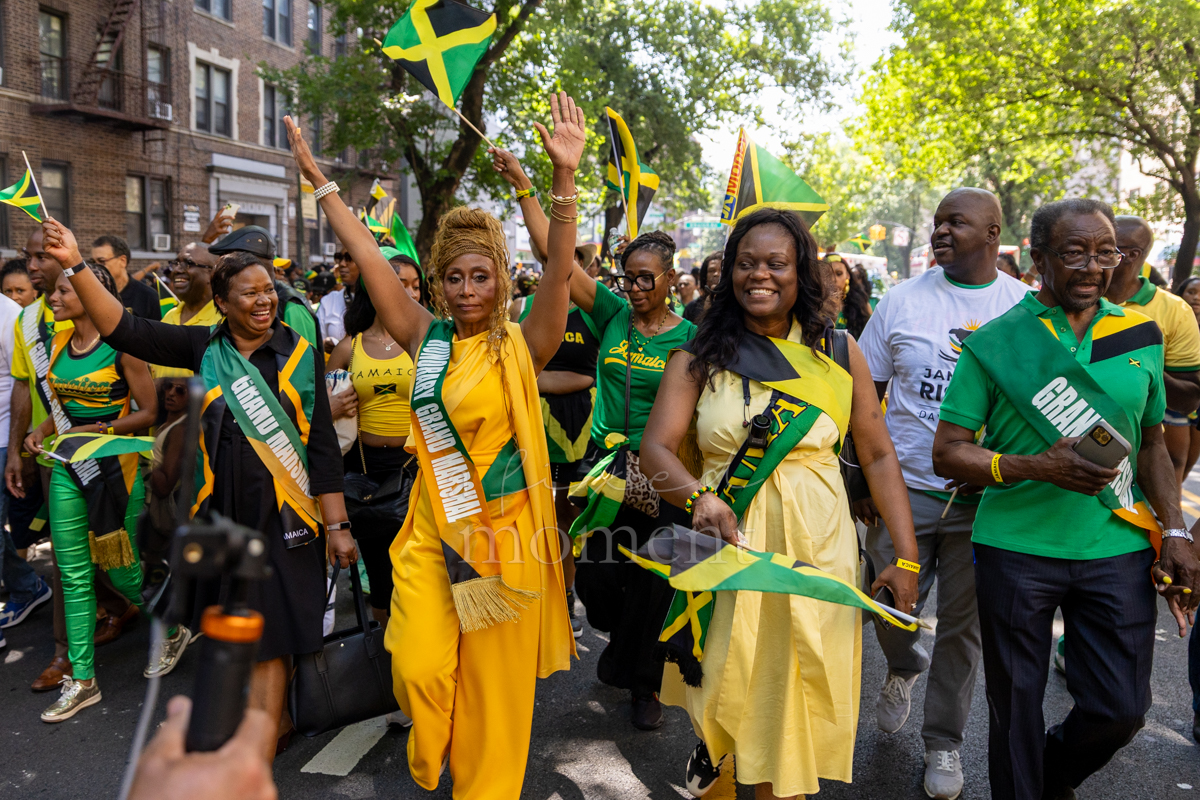 Grand marshals wearing green and gold sashes wave Jamaican flags while walking at the front of the Brooklyn procession