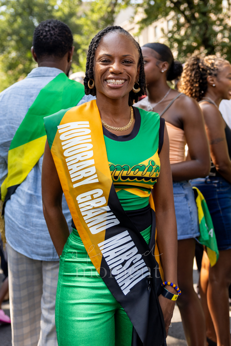 Smiling honorary grand marshal wears a green and gold top, green trousers and a ceremonial sash