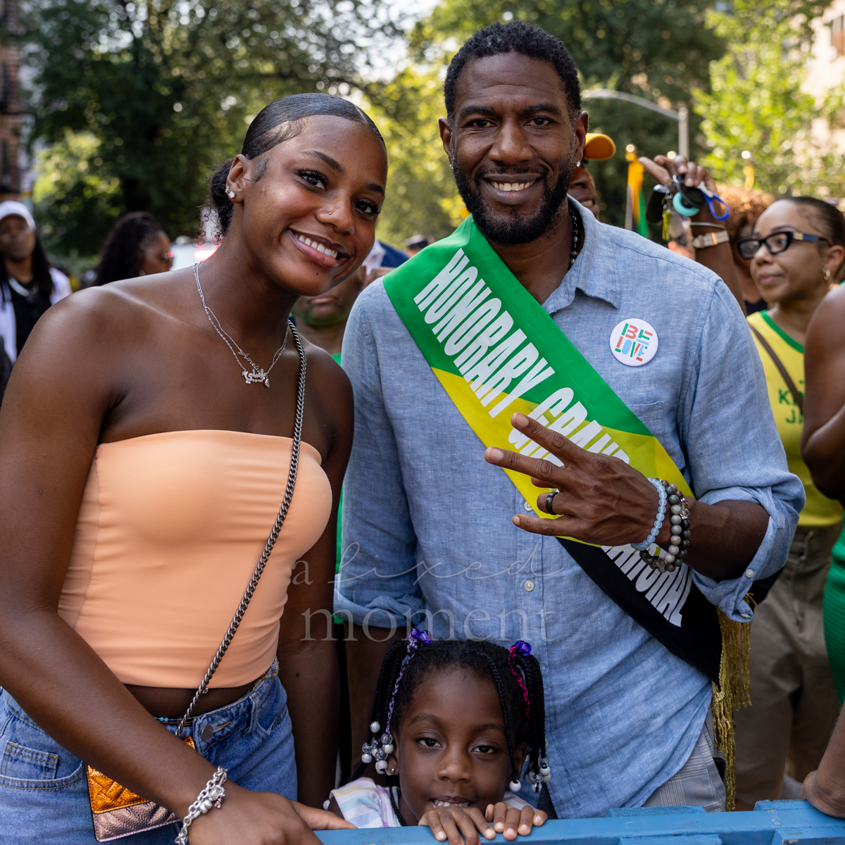 New York City Public Advocate Jumaane D. Williams wears an honorary grand marshal sash and poses with two young attendees