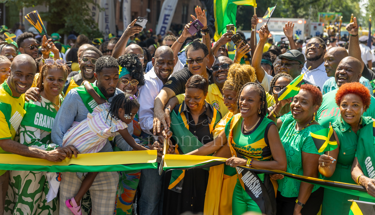 Community leaders, public officials and grand marshals gather around a green, gold and black ribbon during the opening ceremony