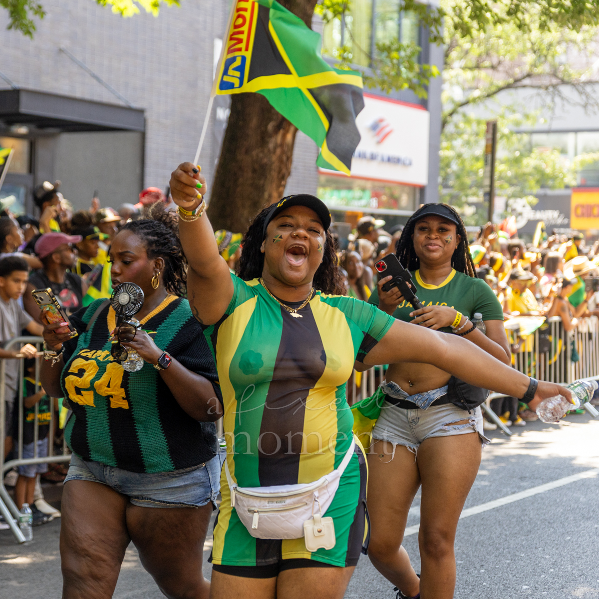 Woman in a green, gold and black romper raises a Jamaican flag with her arms outstretched during the Brooklyn parade