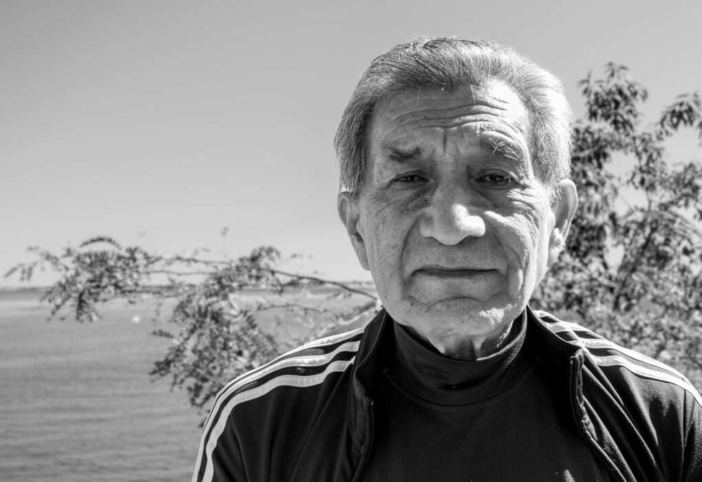 Black-and-white portrait of Pastor Hugo outdoors, with trees and a waterfront in the background.
