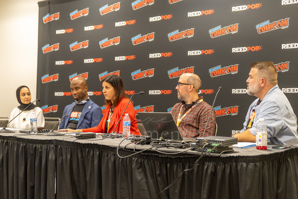 Five participants sit behind microphones during the Know Your Rights panel at New York Comic Con.